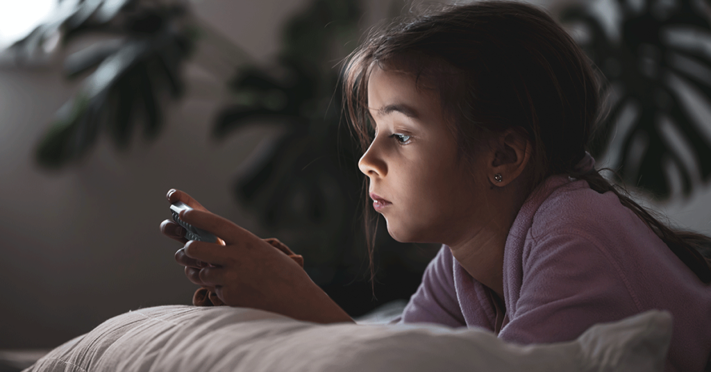 Criança deitada na cama com celular navegando na internet