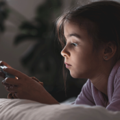 Criança deitada na cama com celular navegando na internet